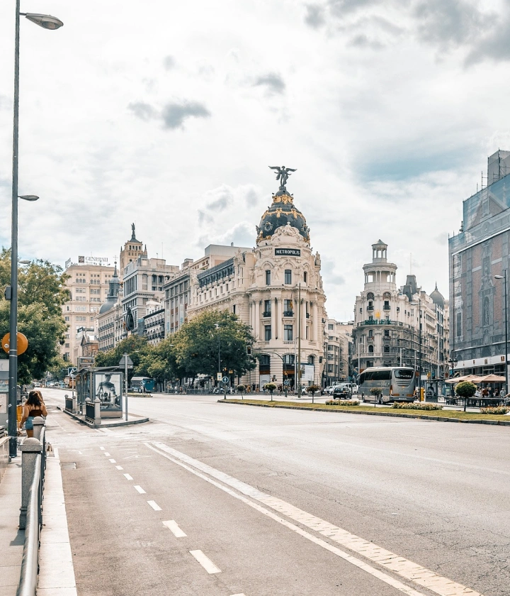 Calle en Madrid con el edificio Metrópolis bajo un cielo nublado.
