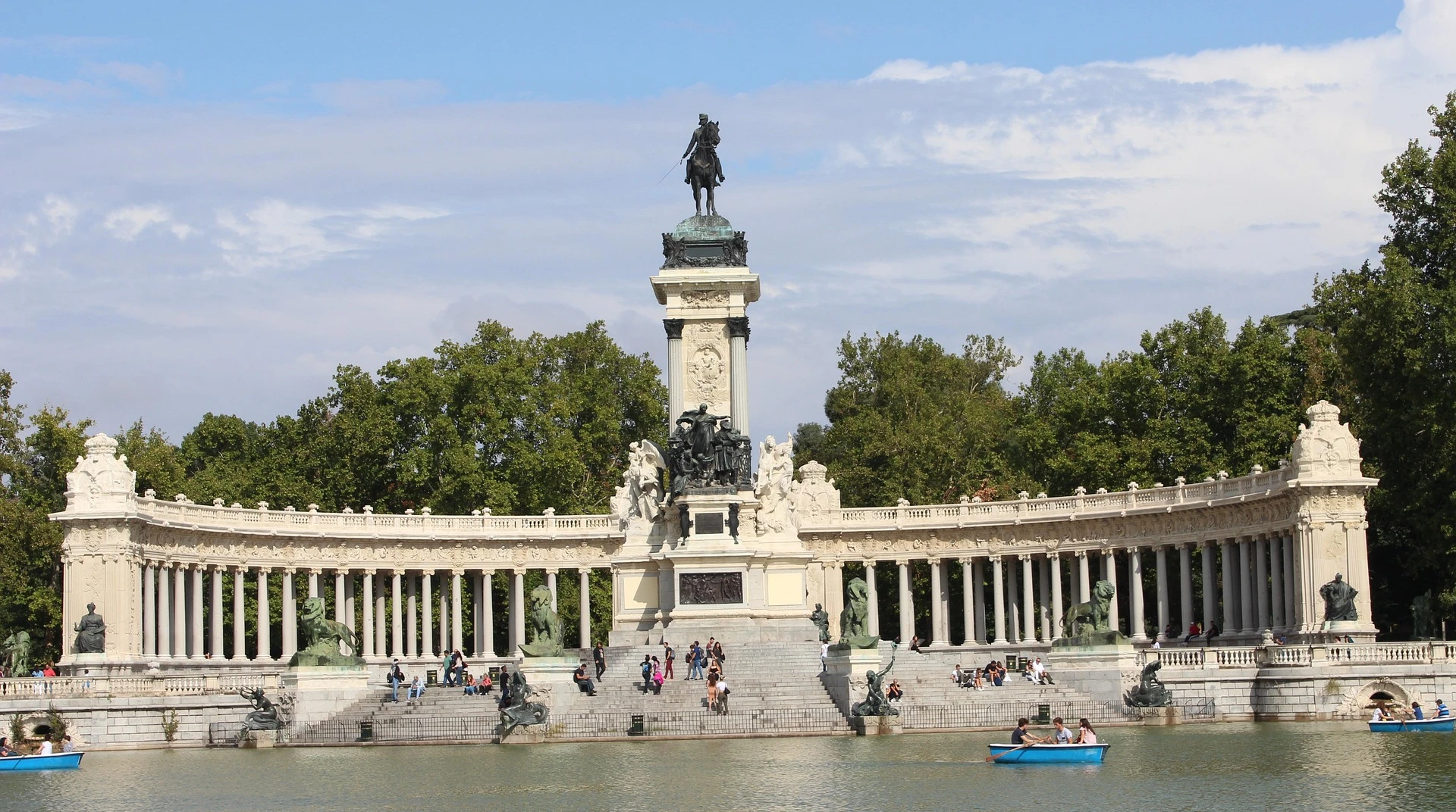 Monumento con columnas y estatua ecuestre en un parque, en un día soleado, con botes en el lago.