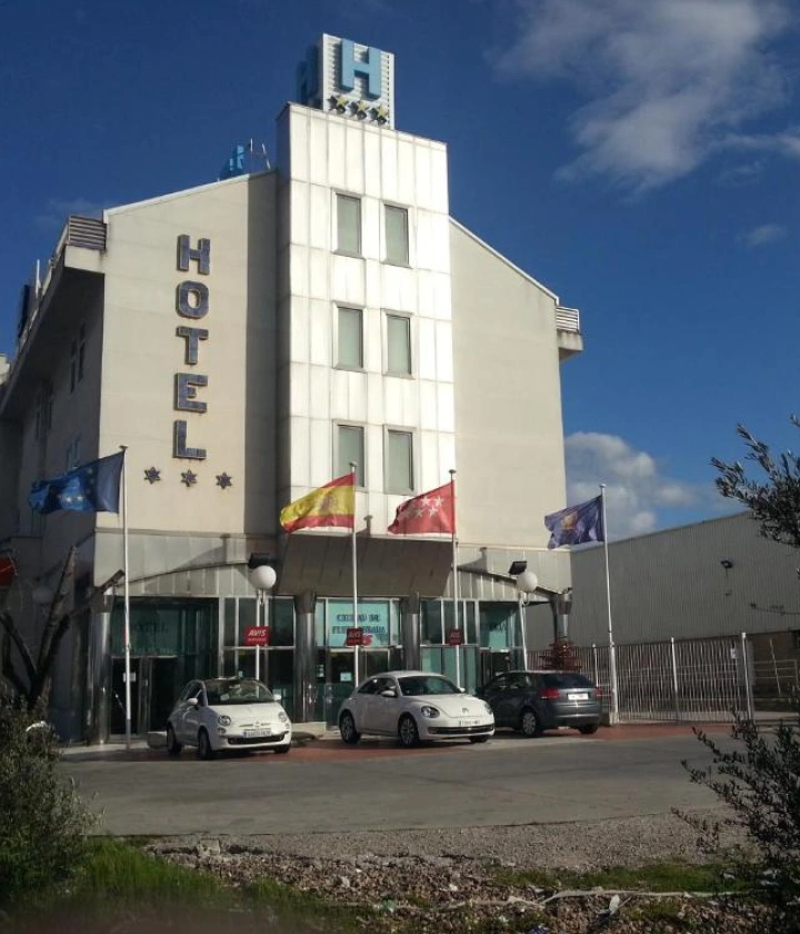 Fachada de hotel moderno con banderas y estacionamiento frente a la entrada principal.