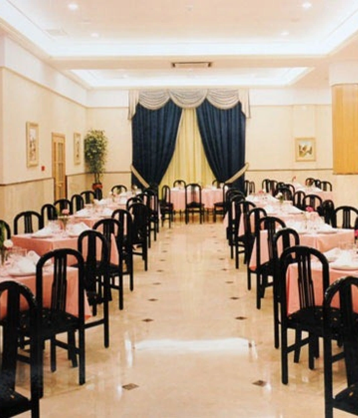 Restaurante elegante con mesas vestidas en rosa y sillas negras, cortinas azules al fondo.