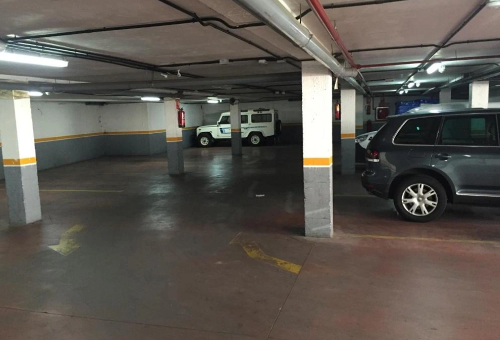 Estacionamiento subterráneo con coches estacionados, columnas y luces en el techo.