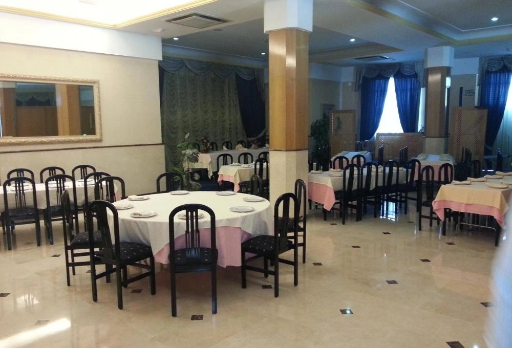 Restaurante elegante con mesas redondas y cuadradas, sillas negras y cortinas azul oscuro.