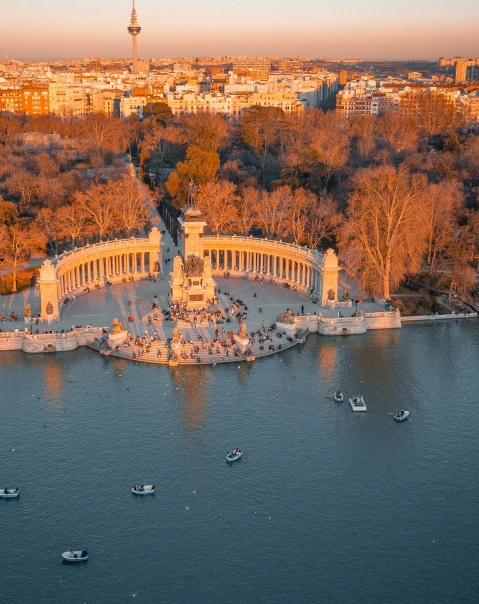 Vista aérea de un monumento junto a un lago, con barcos y árboles al atardecer.