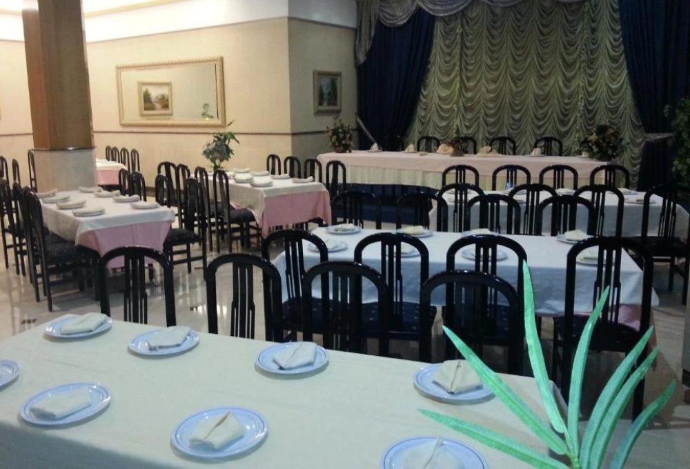 Salón con mesas largas cubiertas y sillas negras, listo para un evento formal.