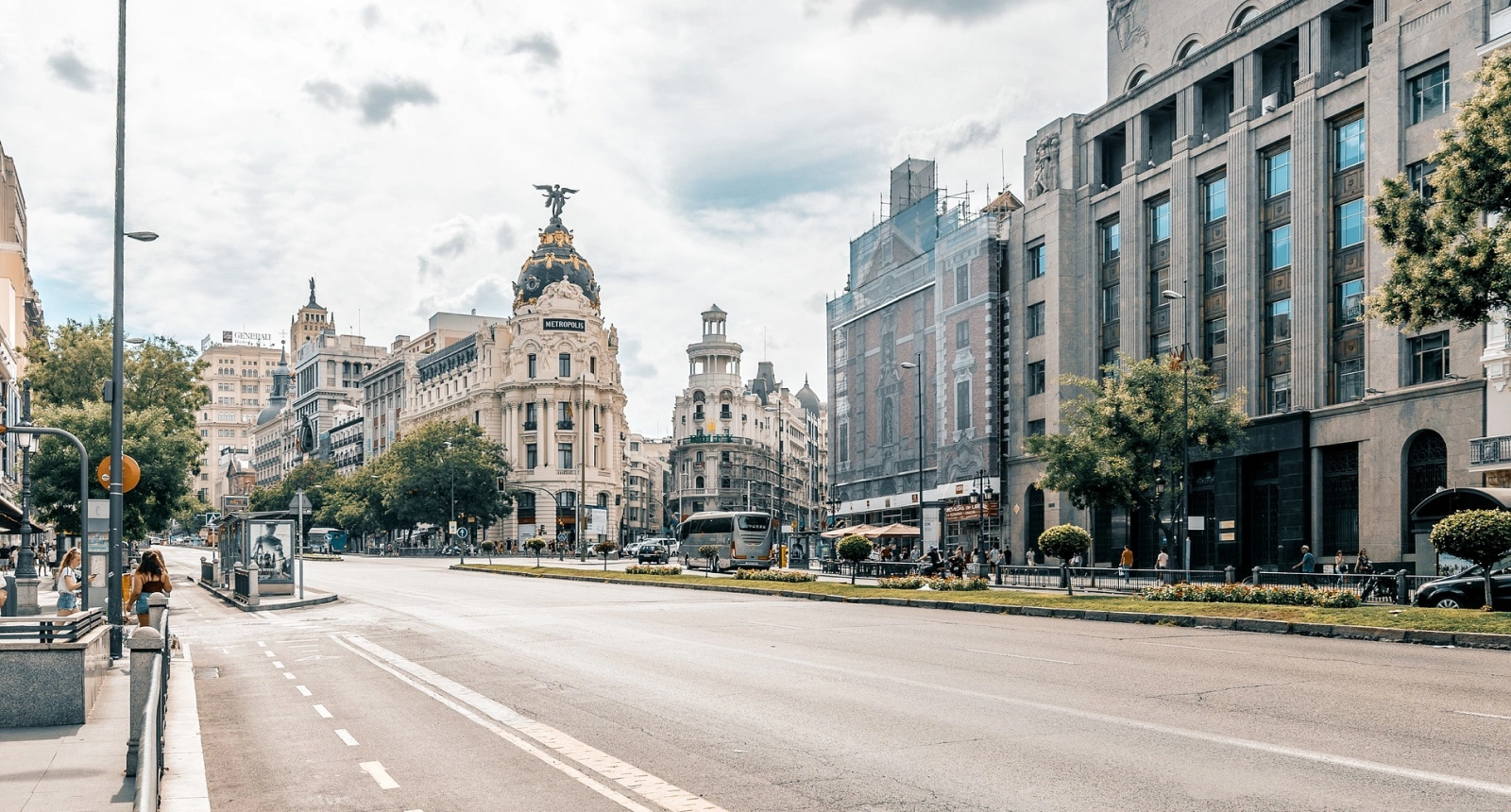 Calle con el edificio Metropolis al fondo, coches y peatones, cielo nublado.