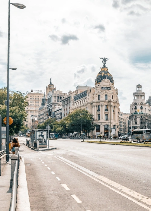 Edificio Metropolis en una avenida amplia y despejada con cielo nublado y árboles a los lados.
