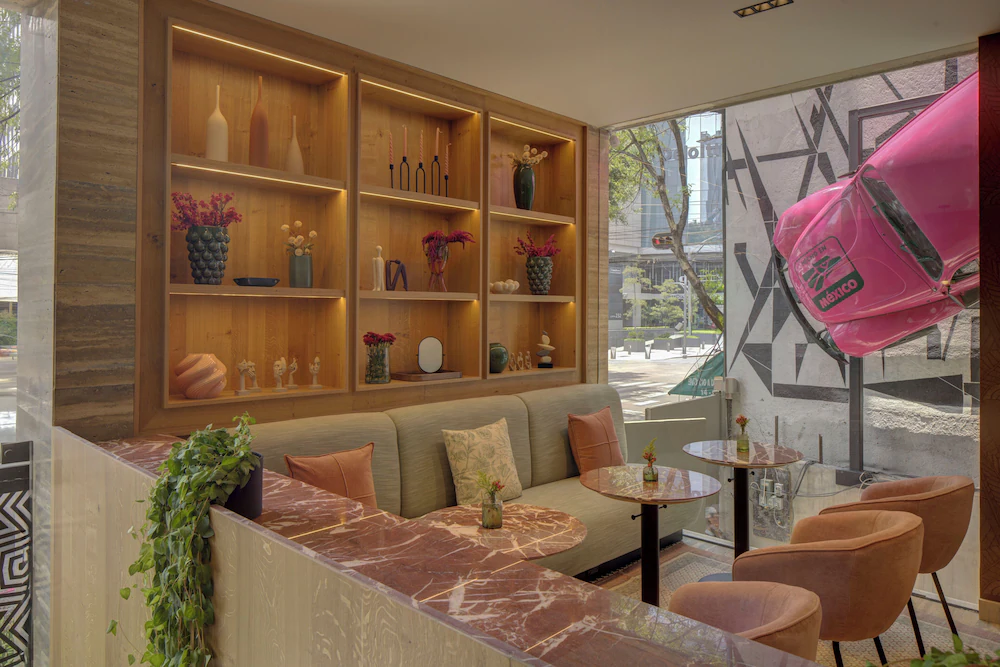Sala moderna con sofás, mesas de mármol, estantería decorativa y un auto rosa empotrado en la pared de vidrio.