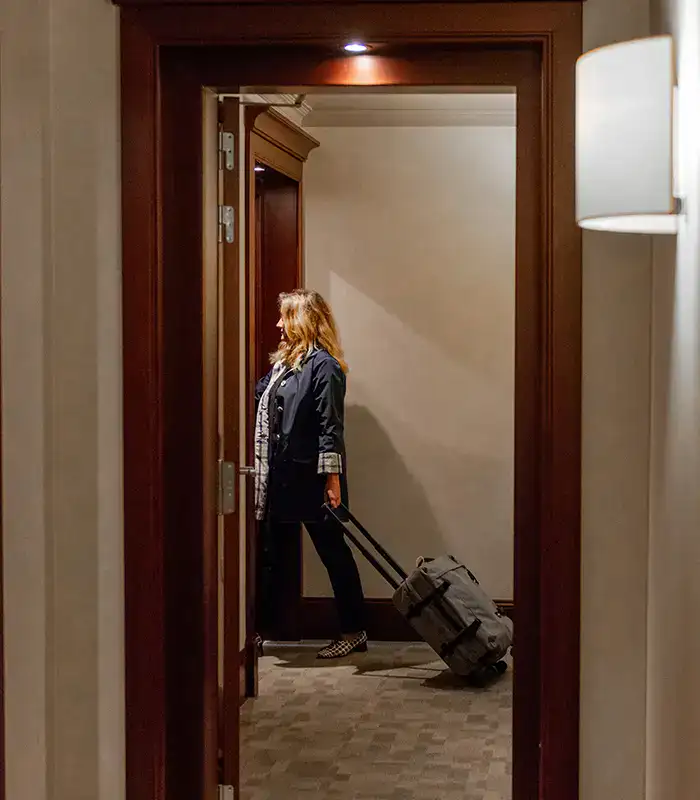 Mujer con abrigo oscuro lleva una maleta por el pasillo de un hotel.