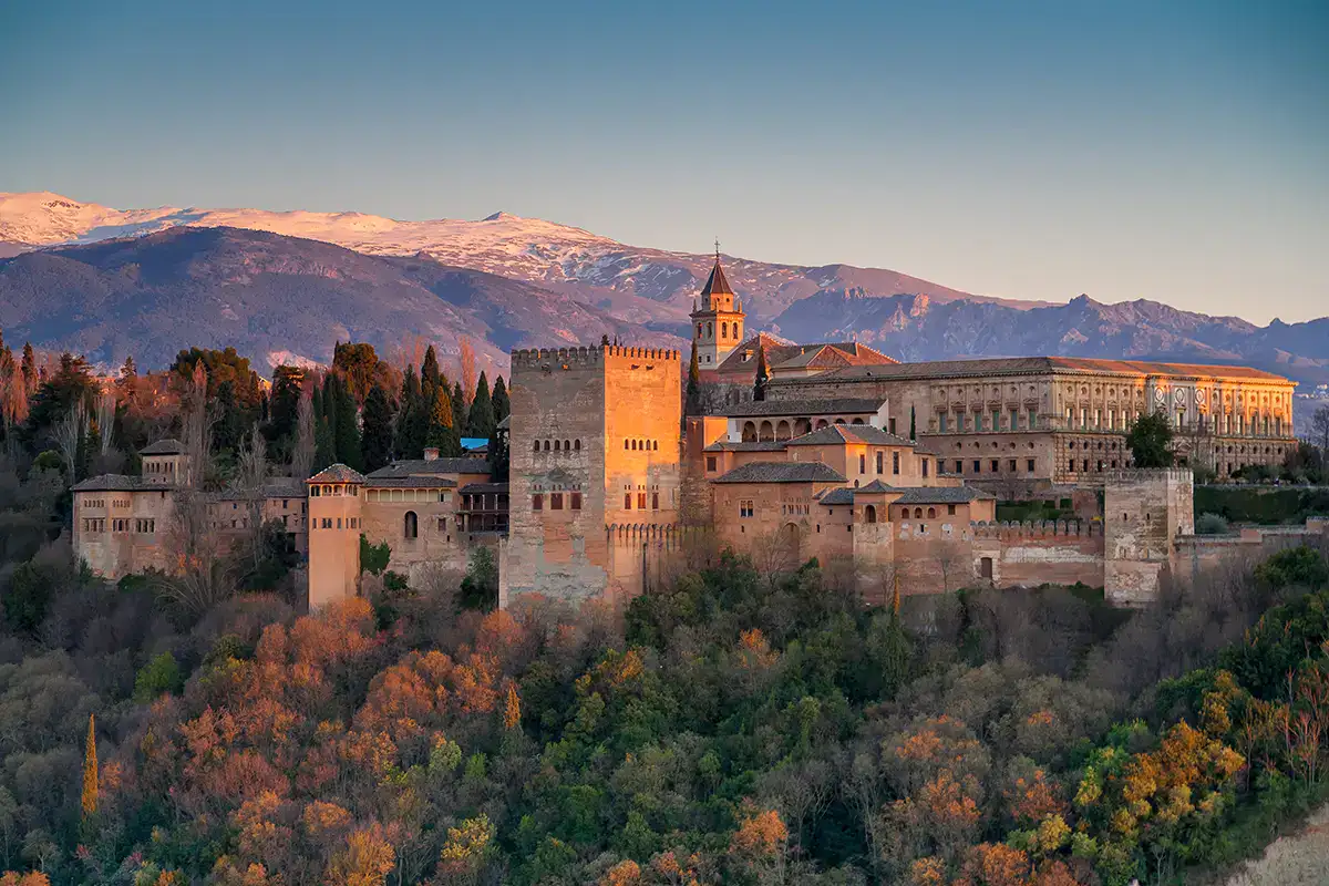 Vista de la Alhambra al atardecer con monta&ntilde;as nevadas al fondo.