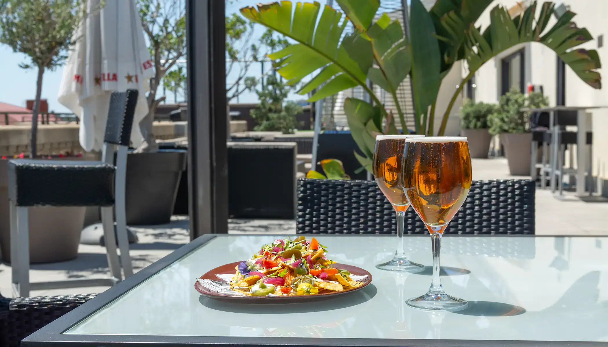 Dos copas de cerveza y nachos en una mesa de terraza soleada.