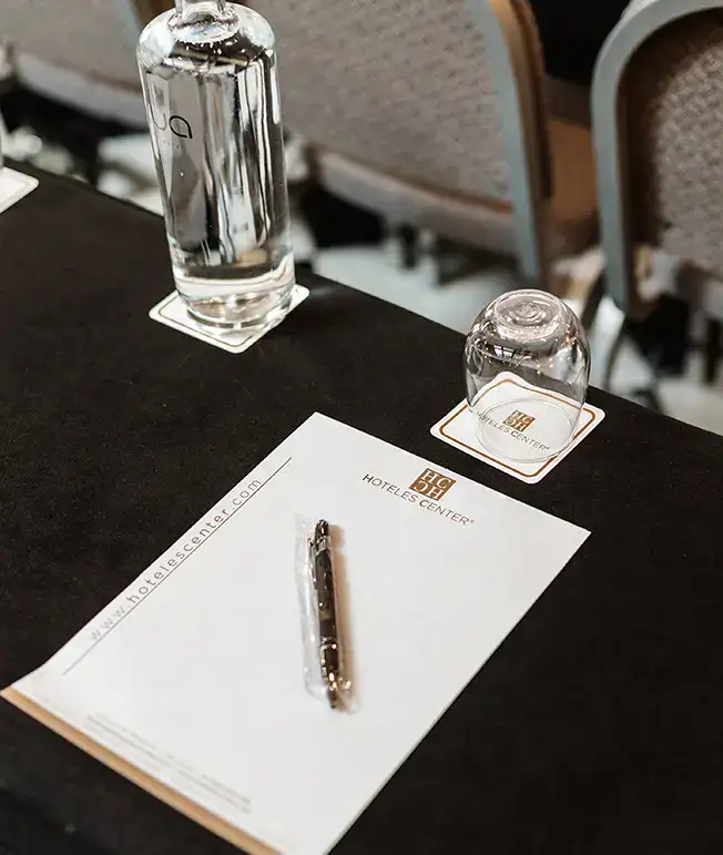 Bloc de notas, bol&iacute;grafo, botella y vaso en mesa de conferencia.