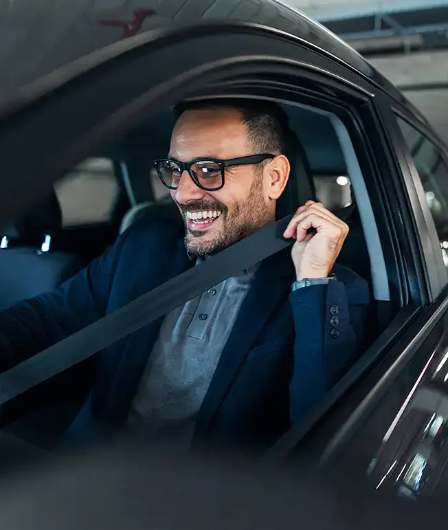 Hombre sonriente poni&eacute;ndose el cintur&oacute;n de seguridad dentro de un coche.