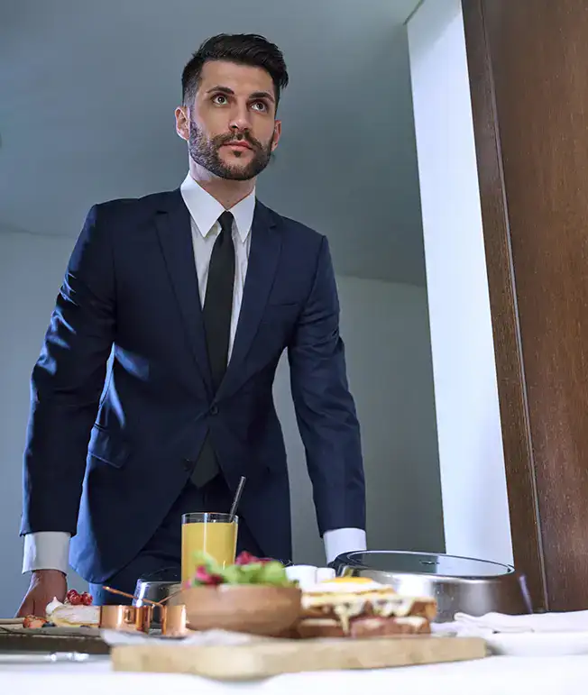 Hombre con traje mirando una mesa con desayuno y jugo de naranja.