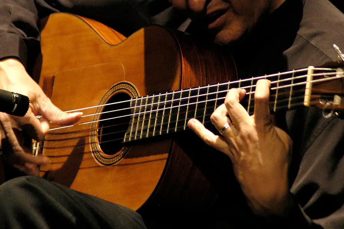 Manos tocando una guitarra cl&aacute;sica con un micr&oacute;fono cerca.