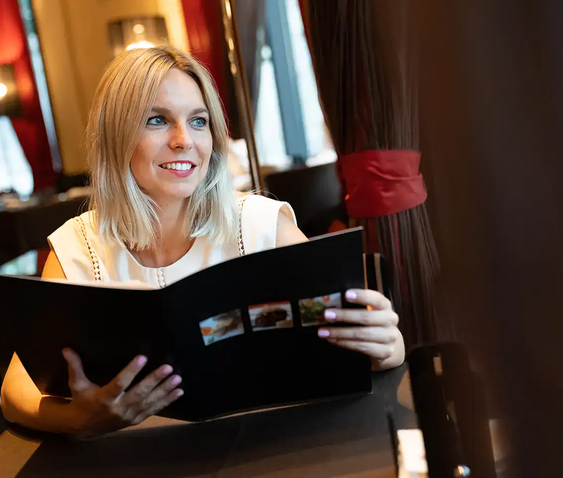 Mujer sonriente en restaurante mirando un men&uacute;.