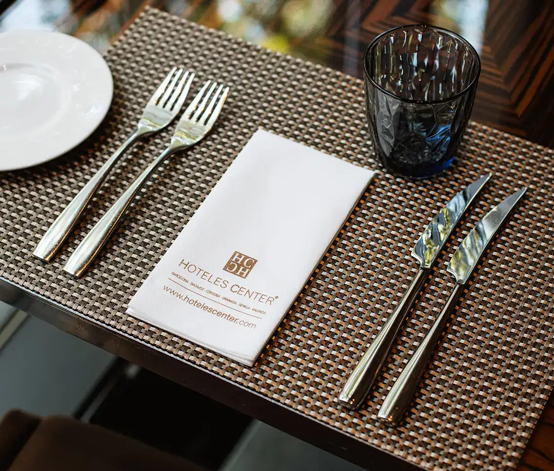 Cubiertos y servilleta de hotel sobre un mantel individual marr&oacute;n.