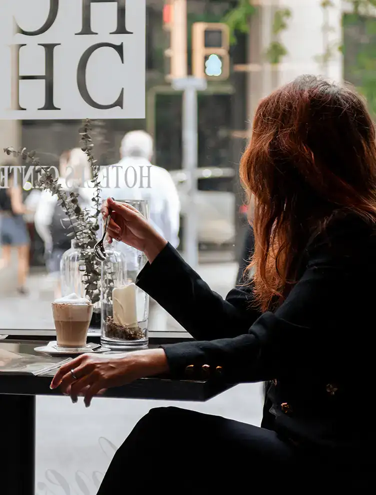 Mujer sentada en una cafeter&iacute;a con un caf&eacute; y flores secas en la mesa.