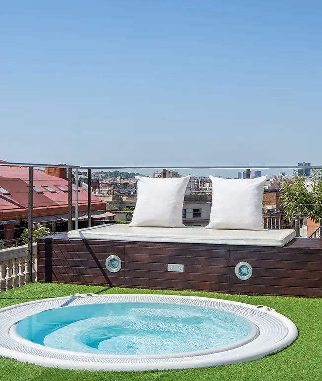 Terraza con jacuzzi y vista a la ciudad, dos cojines blancos sobre un banco.