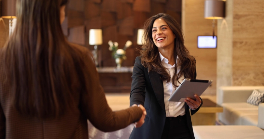 Mujer sonriente estrechando la mano con otra persona, sosteniendo una tablet.