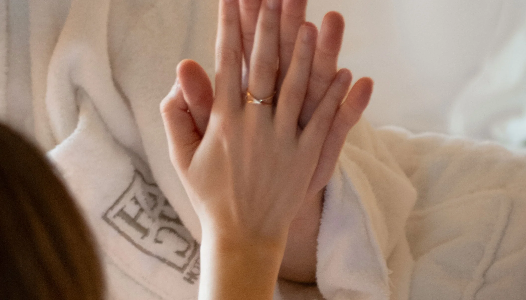 Una mano con anillo est&aacute; sobre otra mano en una bata blanca.