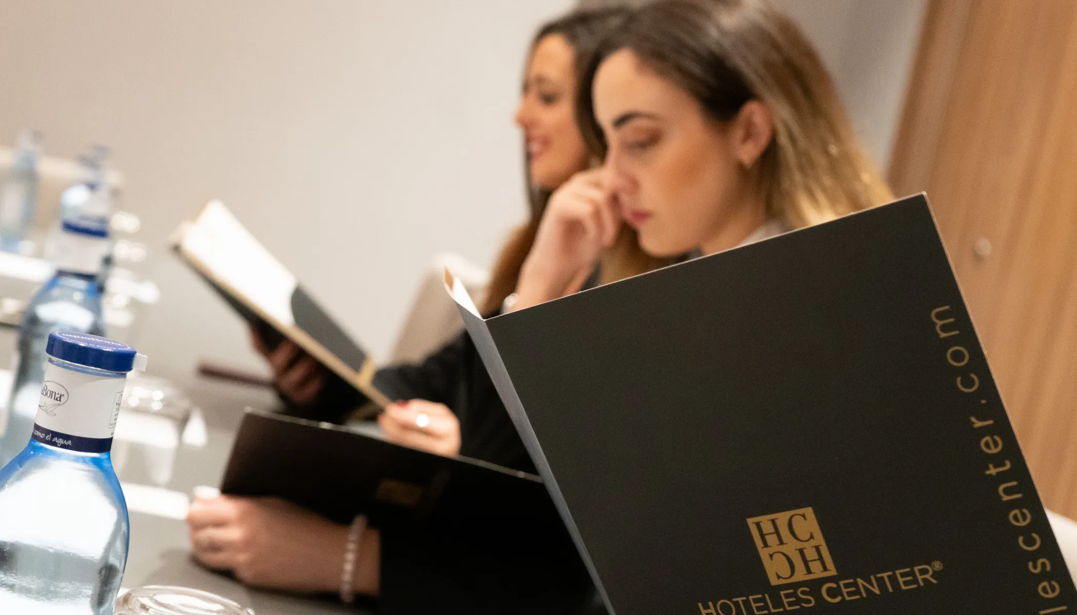 Personas leyendo men&uacute;s en una mesa con botellas de agua.