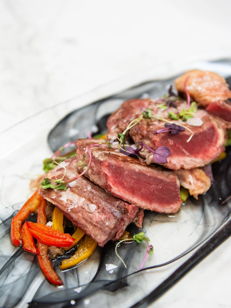 Carne asada en rodajas con pimientos y brotes sobre plato decorado.