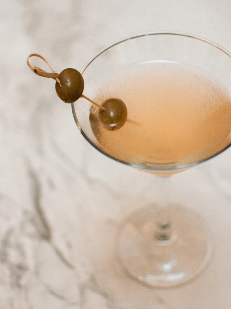 C&oacute;ctel en copa de Martini con aceitunas en un palillo, sobre fondo marmolado.