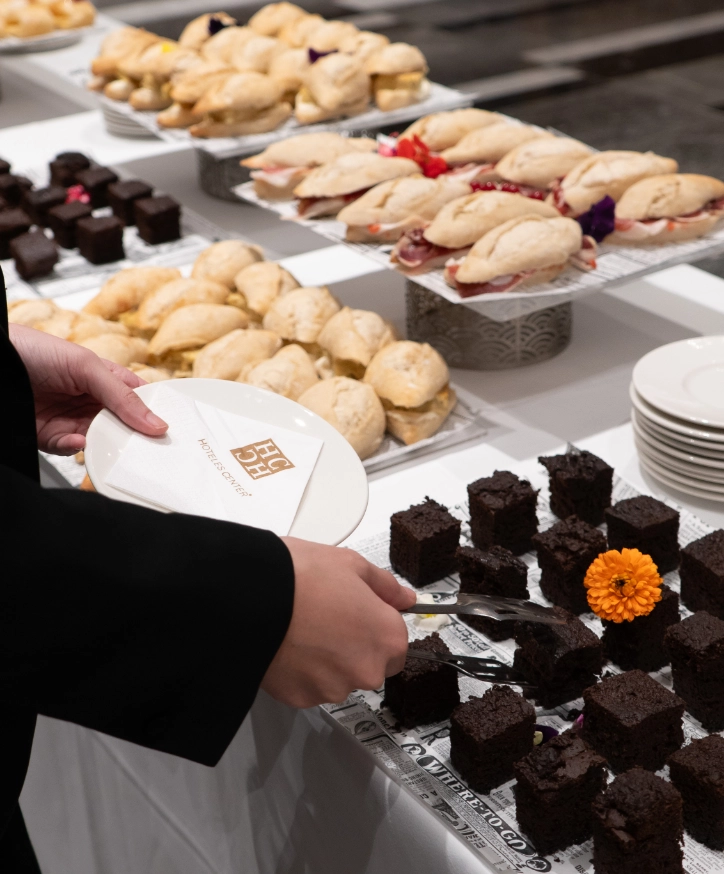 Persona sirve pastel en buffet con s&aacute;ndwiches y bollos.