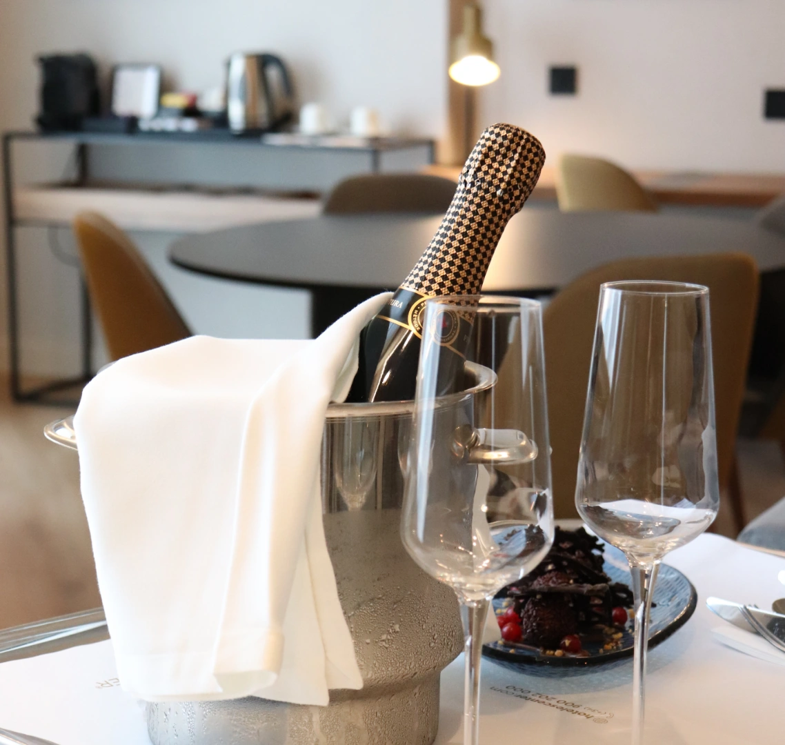 Botella de champ&aacute;n en enfriador junto a copas y postre en una mesa elegante.