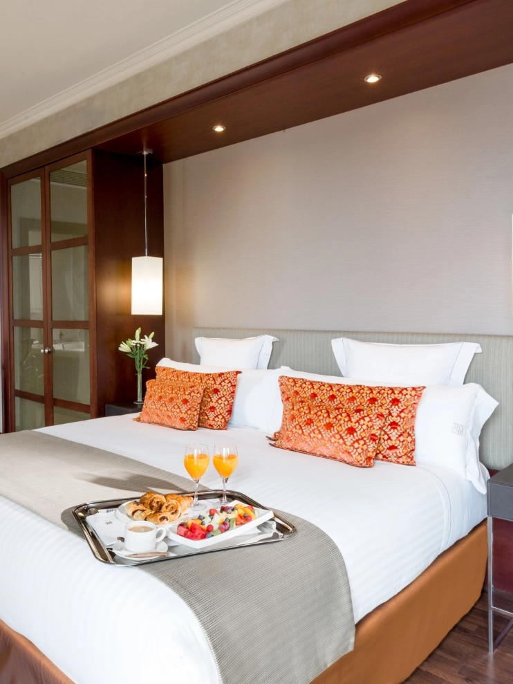 Cama con bandeja de desayuno y cojines naranjas en una habitaci&oacute;n elegante.