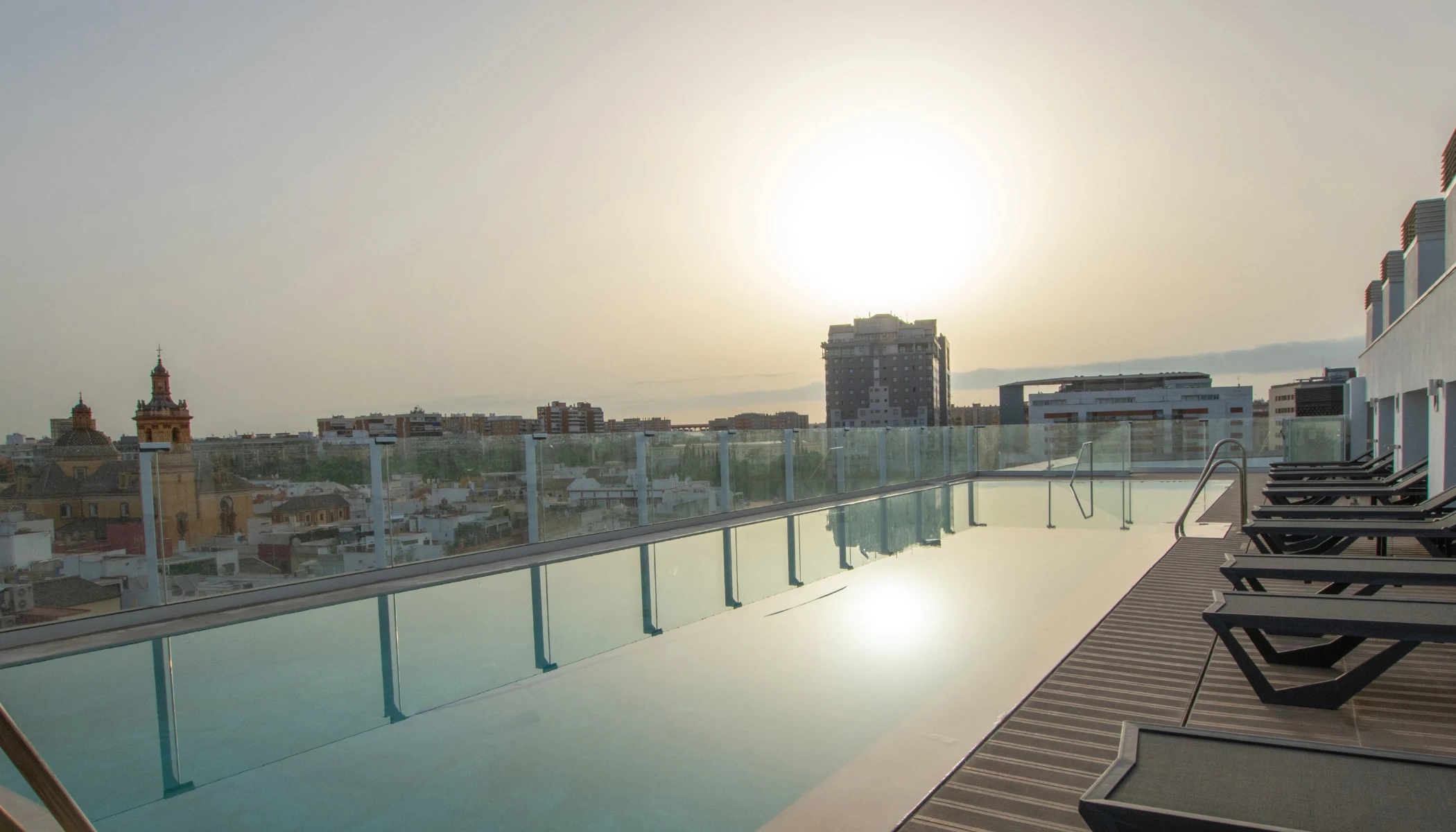 Piscina con tumbonas al atardecer, vista panor&aacute;mica de la ciudad.