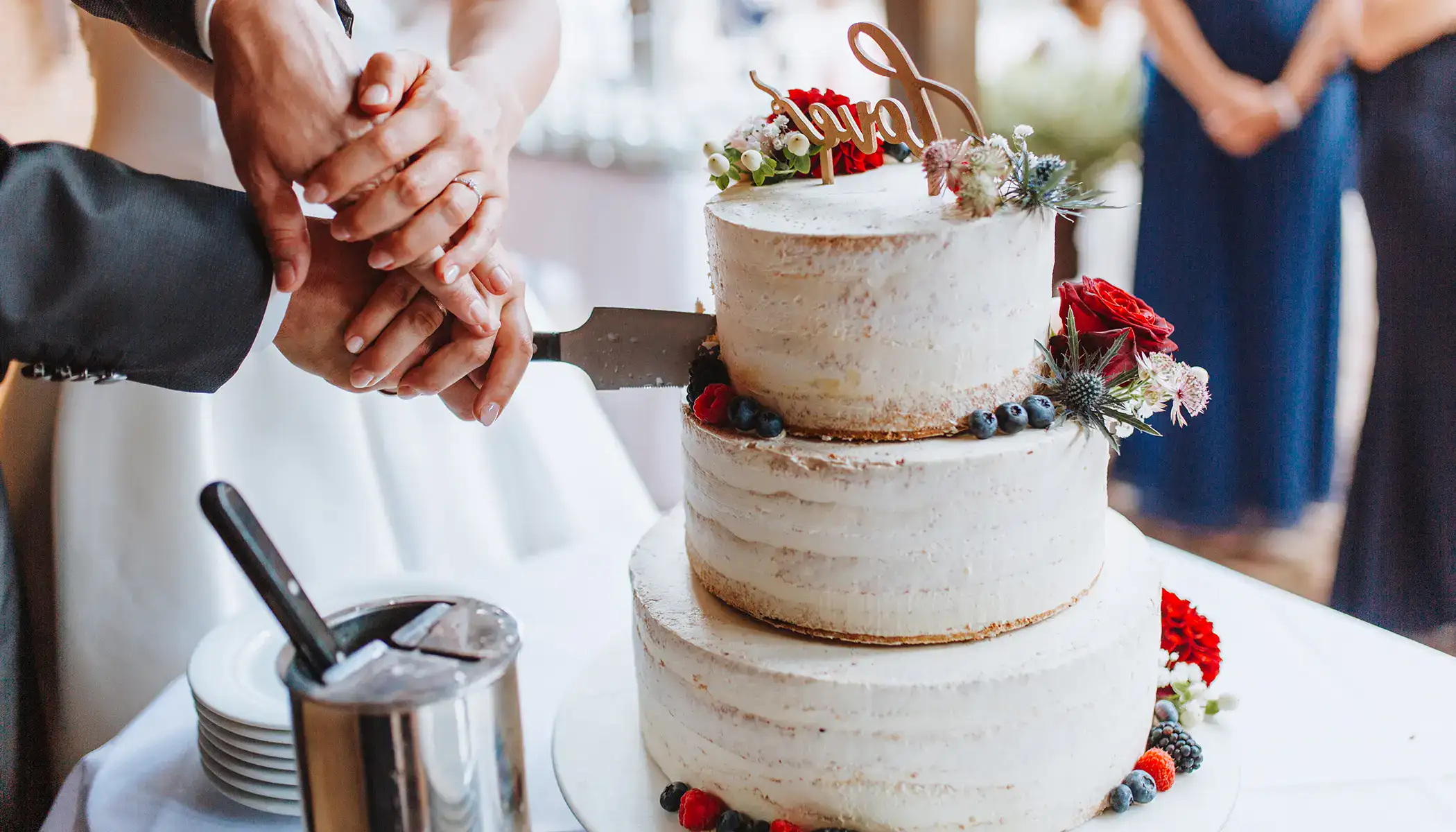 Pareja cortando un pastel de bodas decorado con flores y frutas.