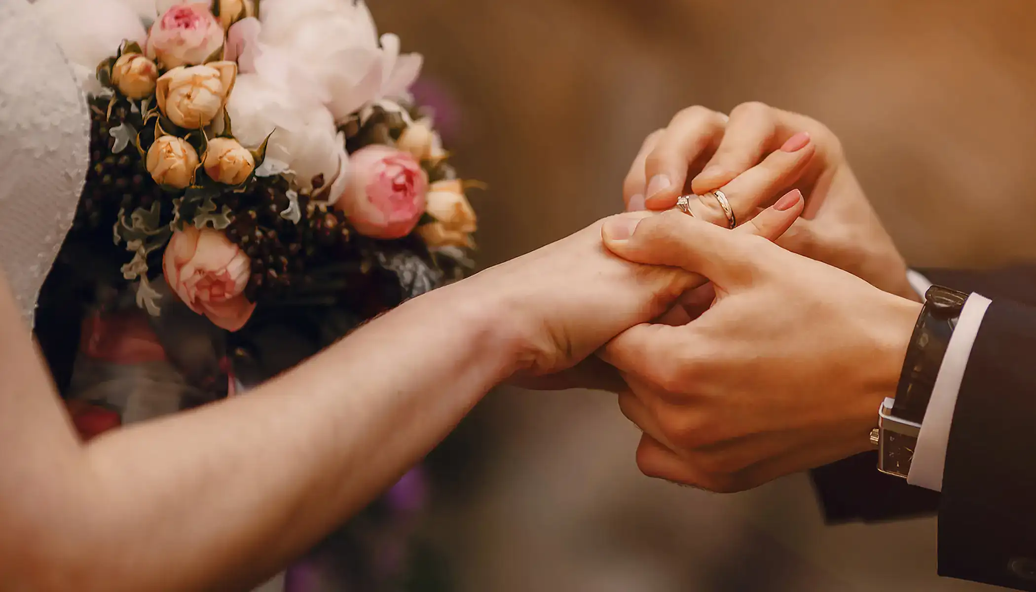 Pareja intercambiando anillos de boda junto a ramo de flores.