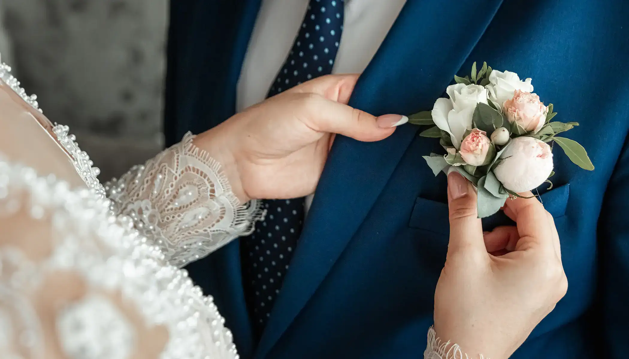 Novia ajustando boutonnieres en traje azul del novio.