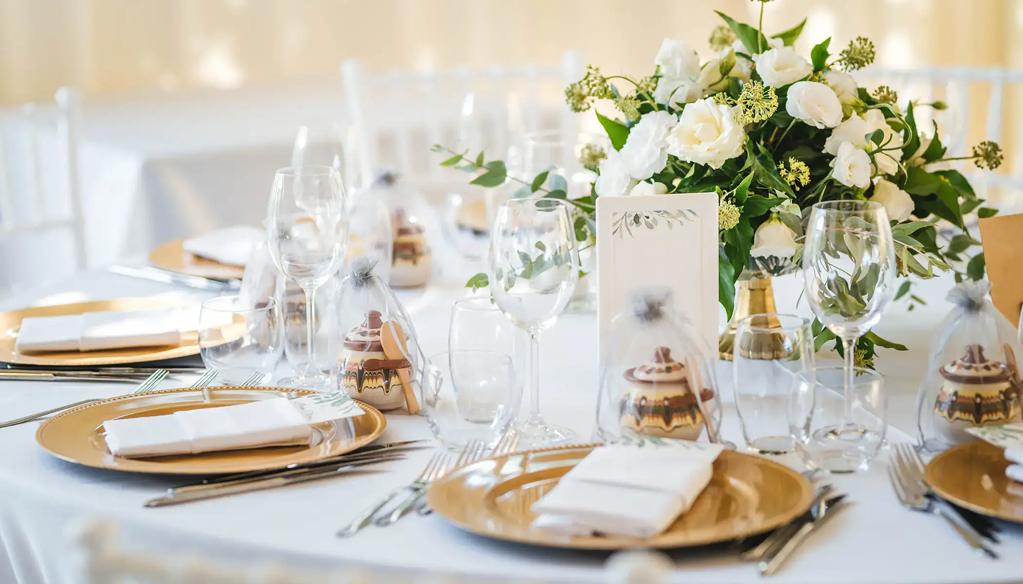 Mesa elegante con vajilla dorada y centro de flores blancas y verdes.