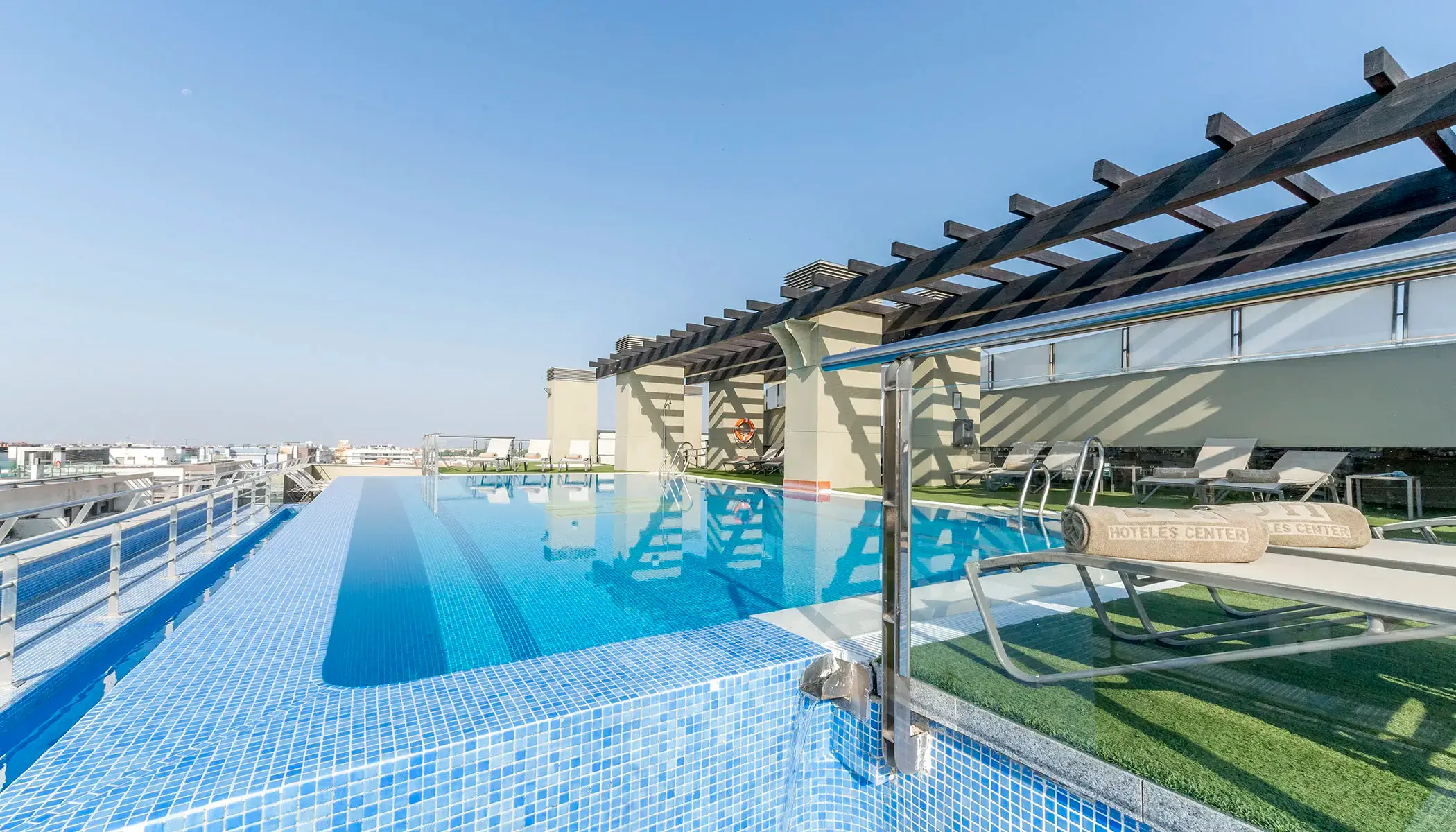 Piscina infinita en la azotea con tumbonas y cielo despejado.