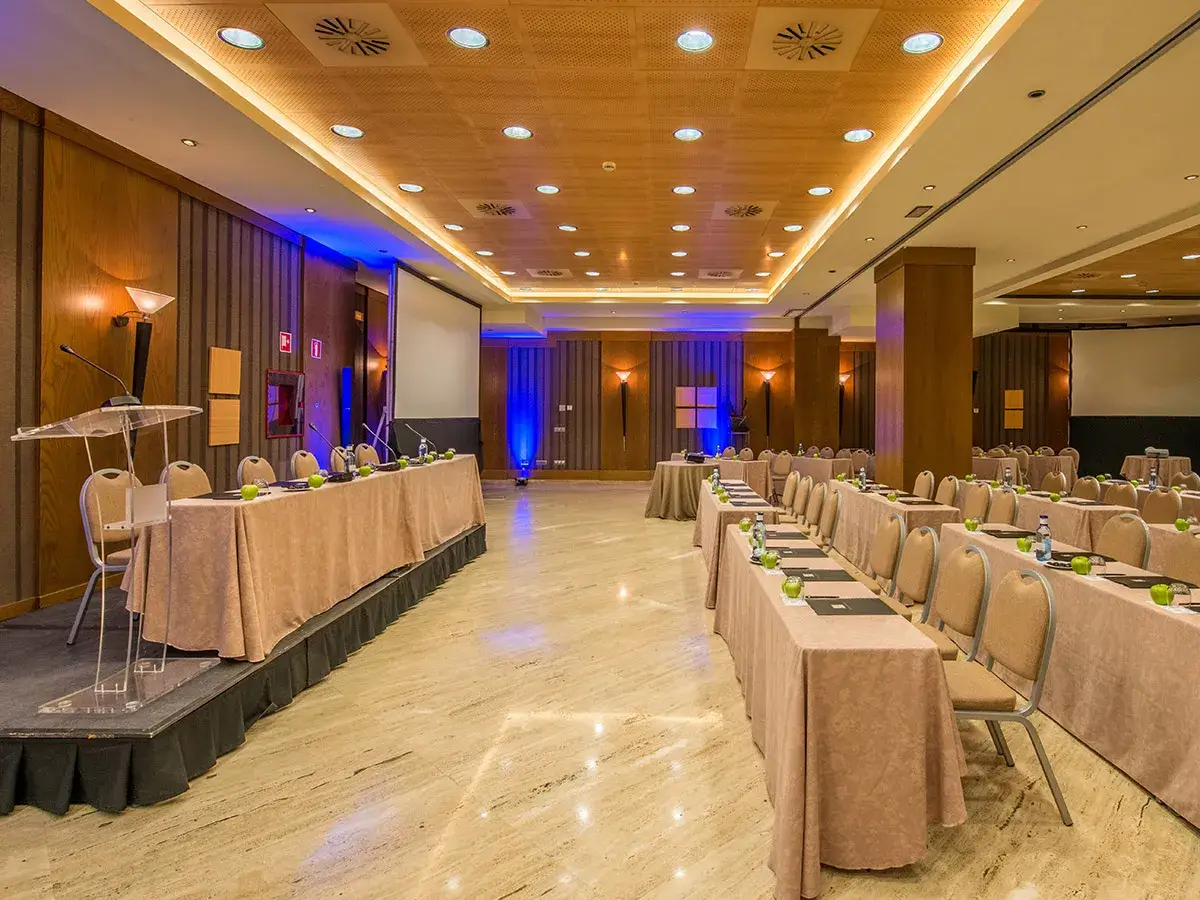 Sala de conferencias con mesas cubiertas, sillas y proyector en el fondo.