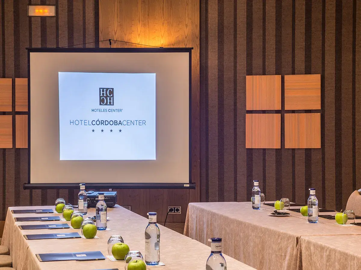 Sala de conferencias del Hotel C&oacute;rdoba Center con mesas, manzanas y agua.