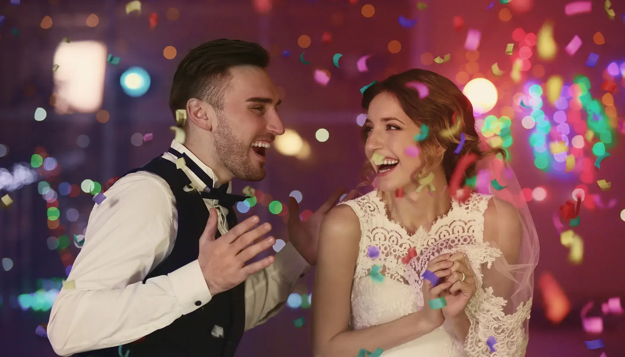 Pareja de novios riendo con confeti colorido cayendo sobre ellos.