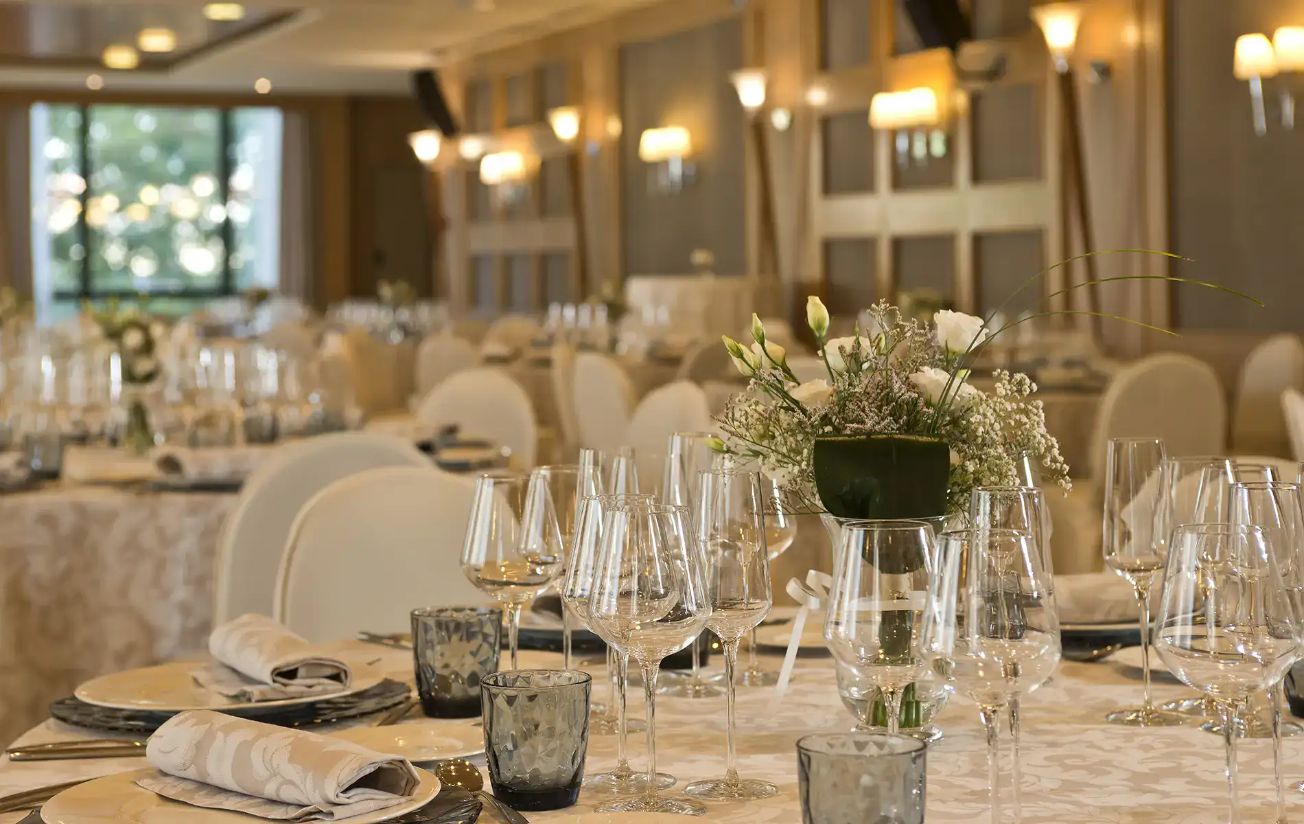 Mesas elegantes con cristaler&iacute;a y flores en un sal&oacute;n iluminado.