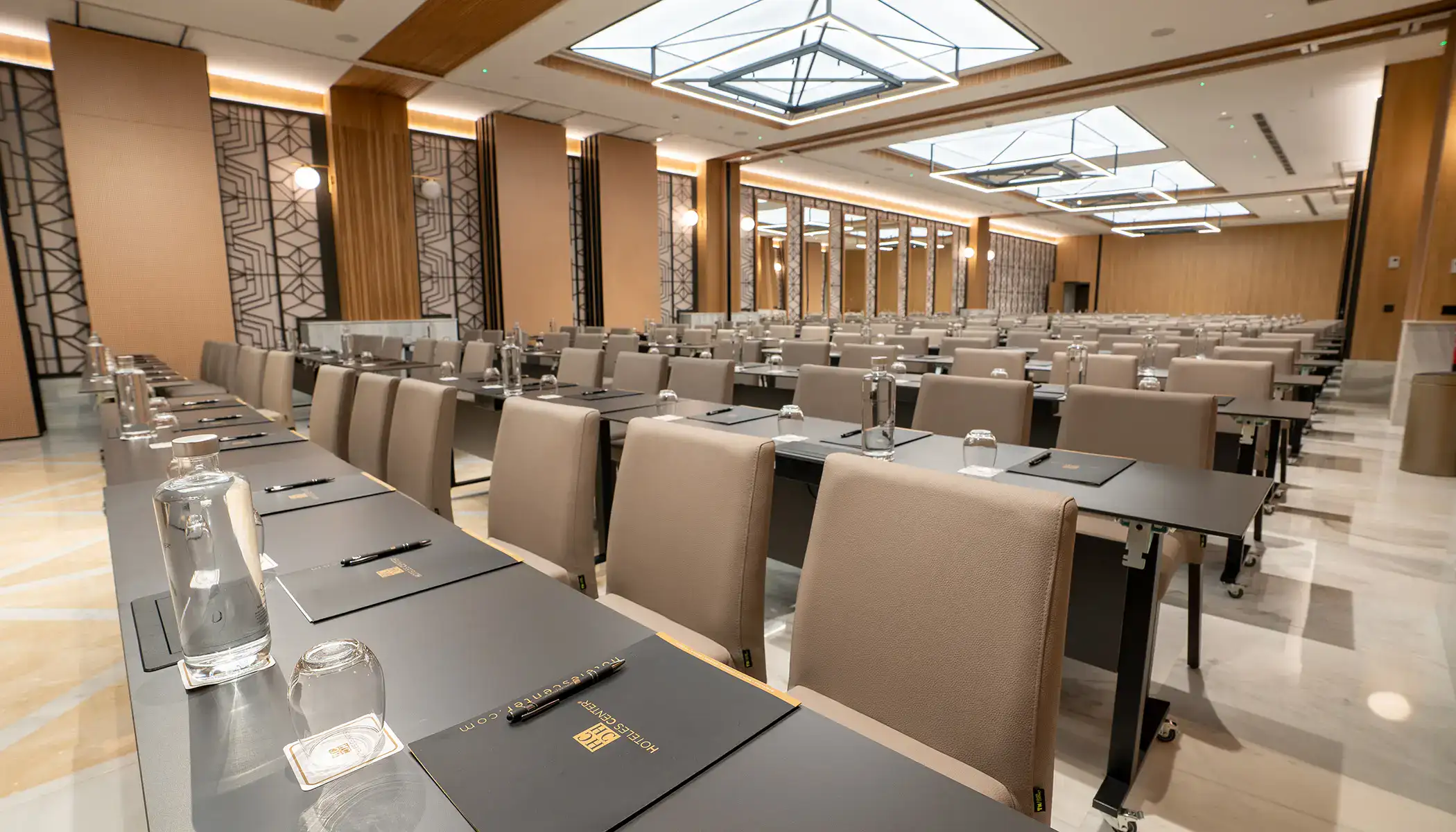 Sala de conferencias vac&iacute;a con mesas, sillas y botellas de agua.