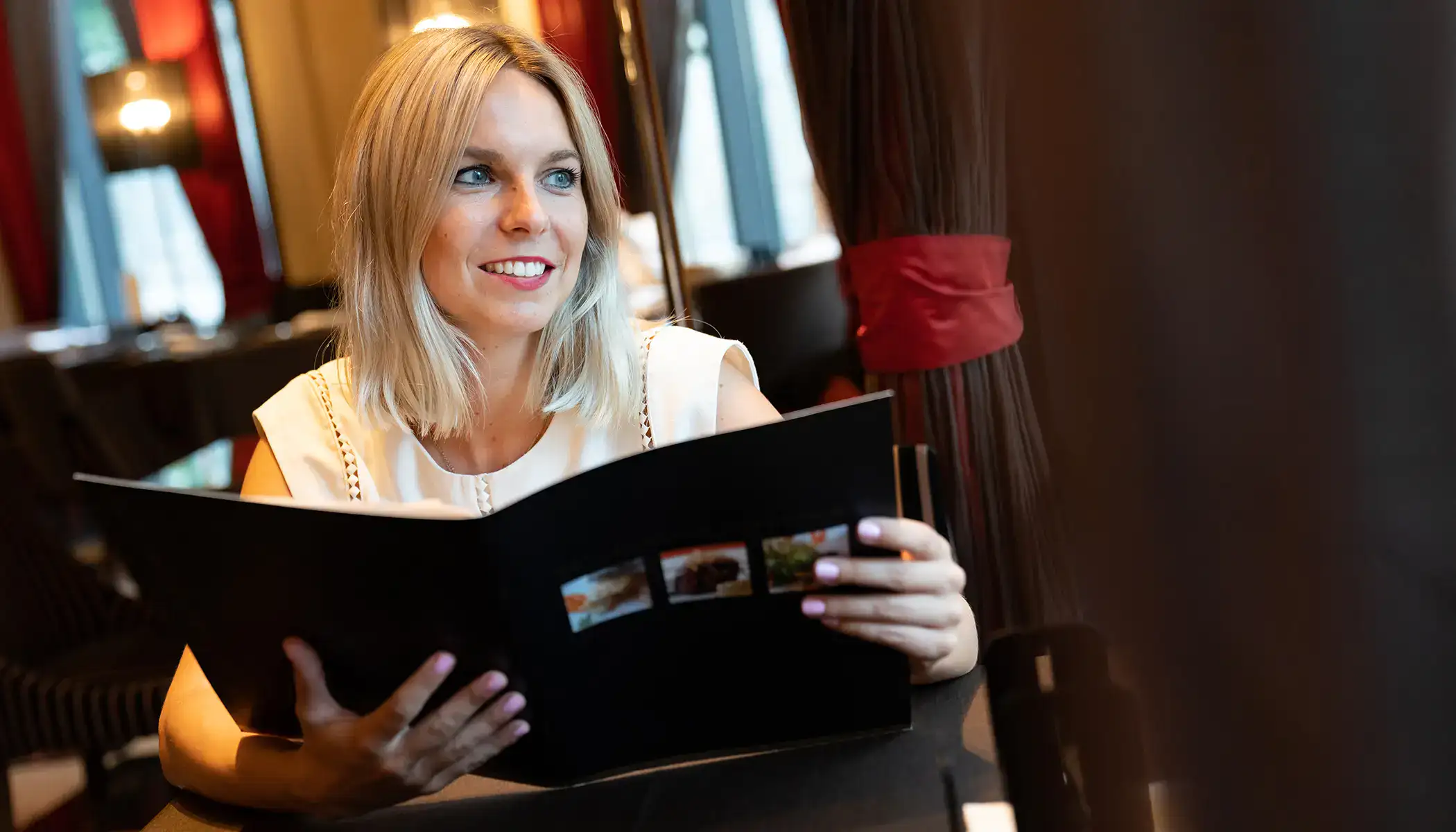 Mujer sonriendo mientras revisa el men&uacute; en un restaurante elegante.