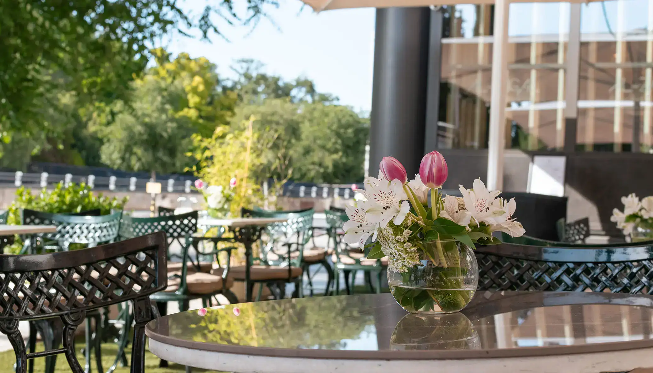 Mesa de caf&eacute; al aire libre con florero y sillas en un entorno verde.