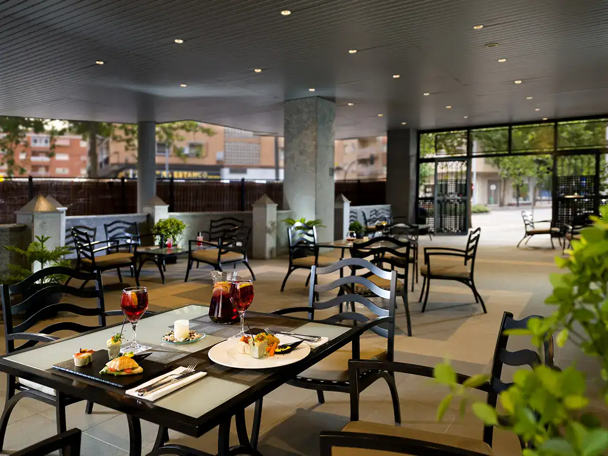Terraza de restaurante con mesas, sillas y comida servida.