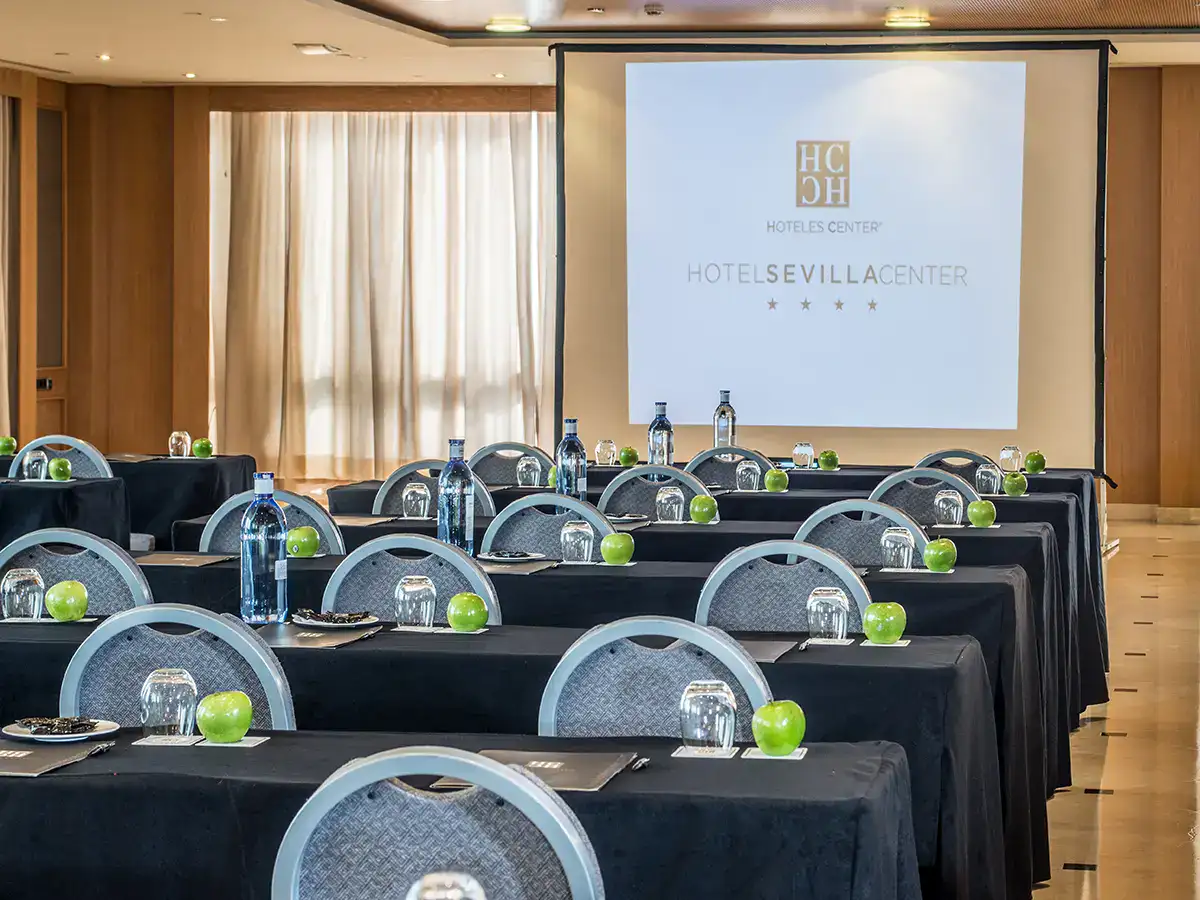 Sala de conferencias con mesas listas y proyector encendido.