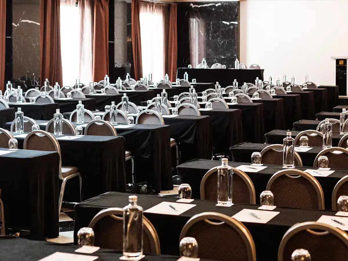 Sala de conferencias con mesas, sillas y botellas de agua.