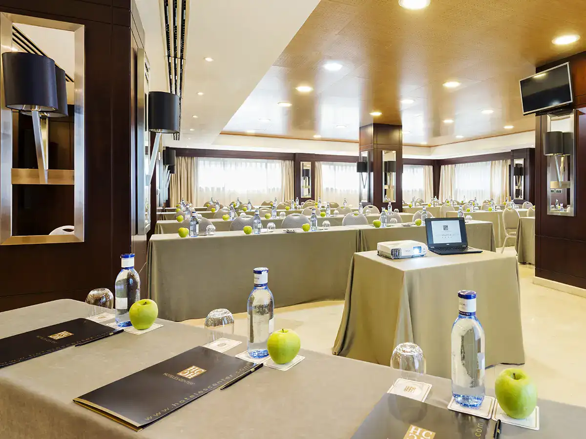Sala de conferencias con mesas, proyectores, manzanas y botellas de agua.