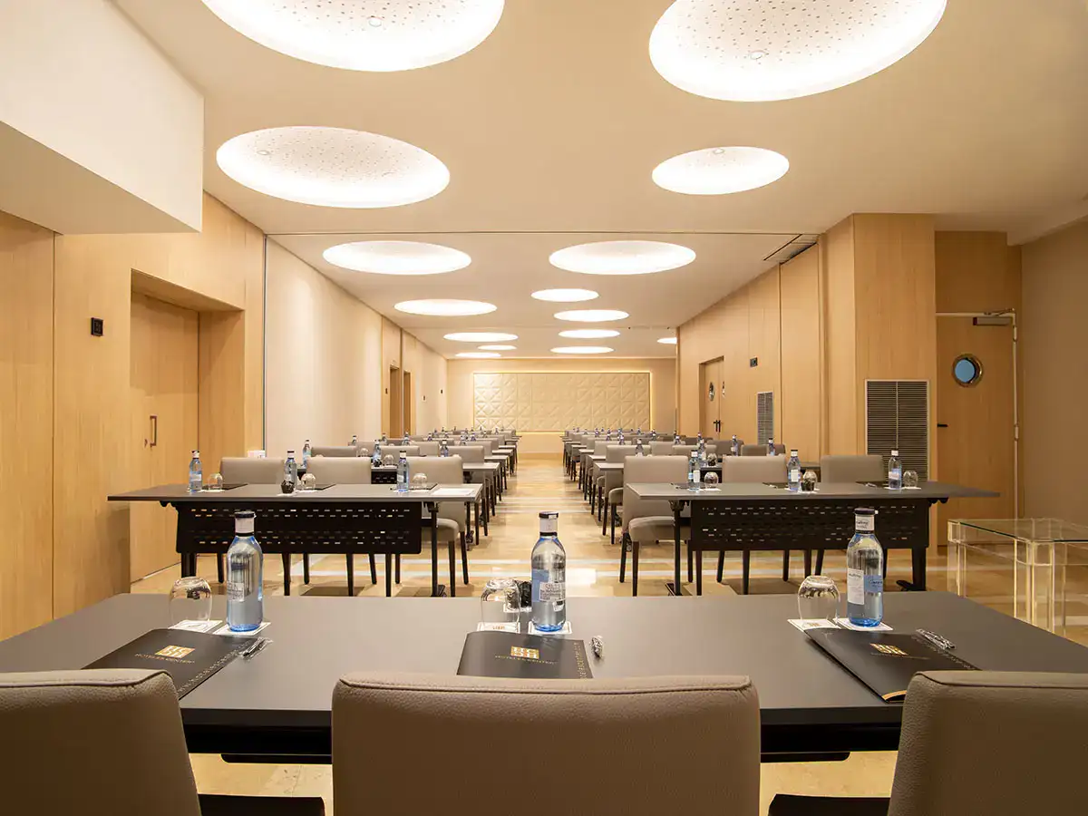 Sala de conferencias vac&iacute;a con mesas grises y botellas de agua.