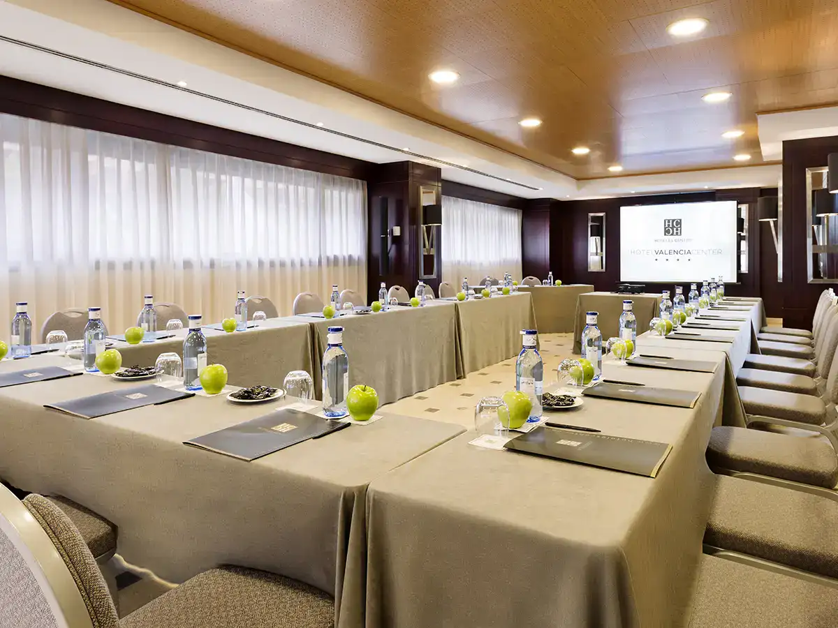 Sala de conferencias con mesas, agua, cuadernos y manzanas verdes.