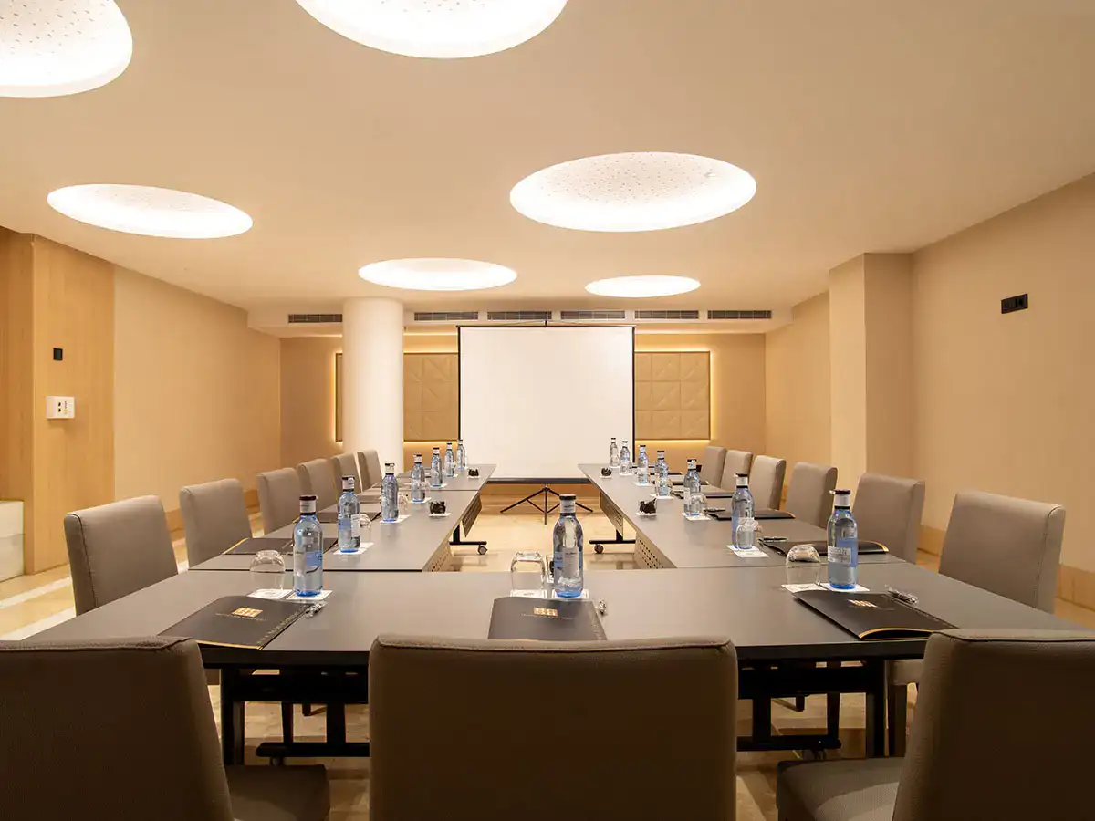 Sala de conferencias con sillas, mesa, botellas de agua y pantalla.